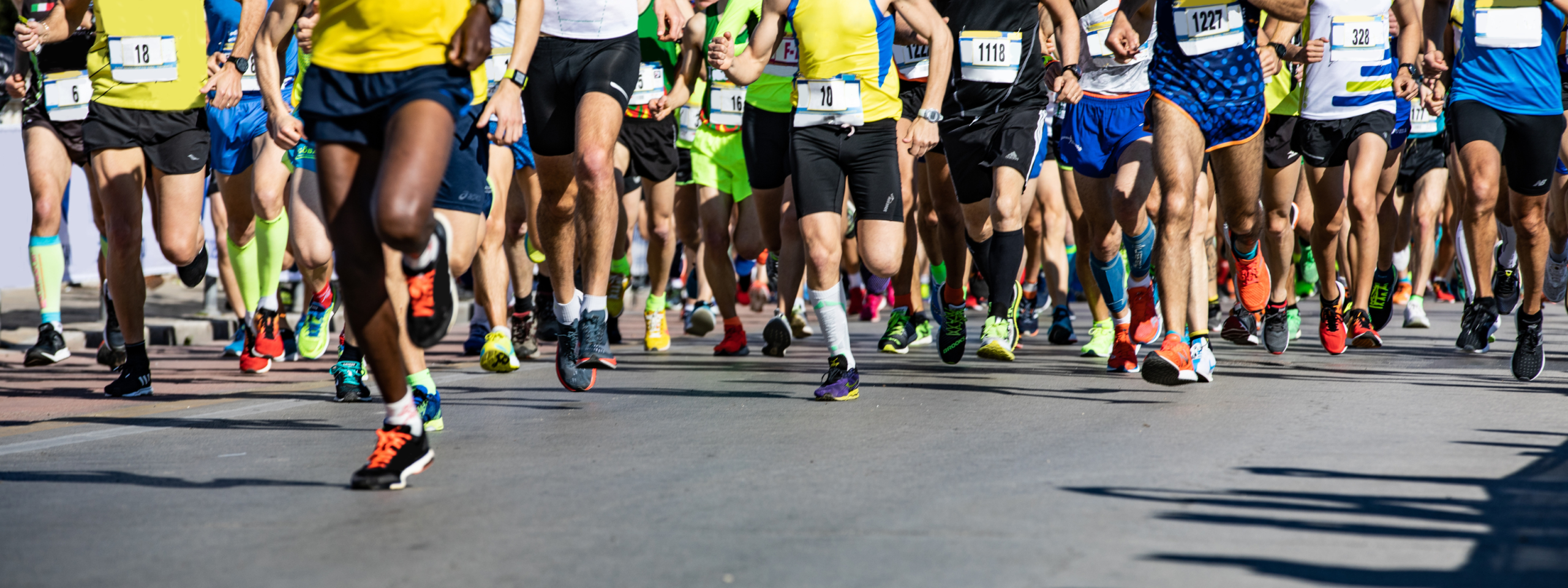 London Marathon A large group of runners in colorful athletic gear participate in a road race, likely a marathon, with focus on their legs and shoes as they run on a paved street.