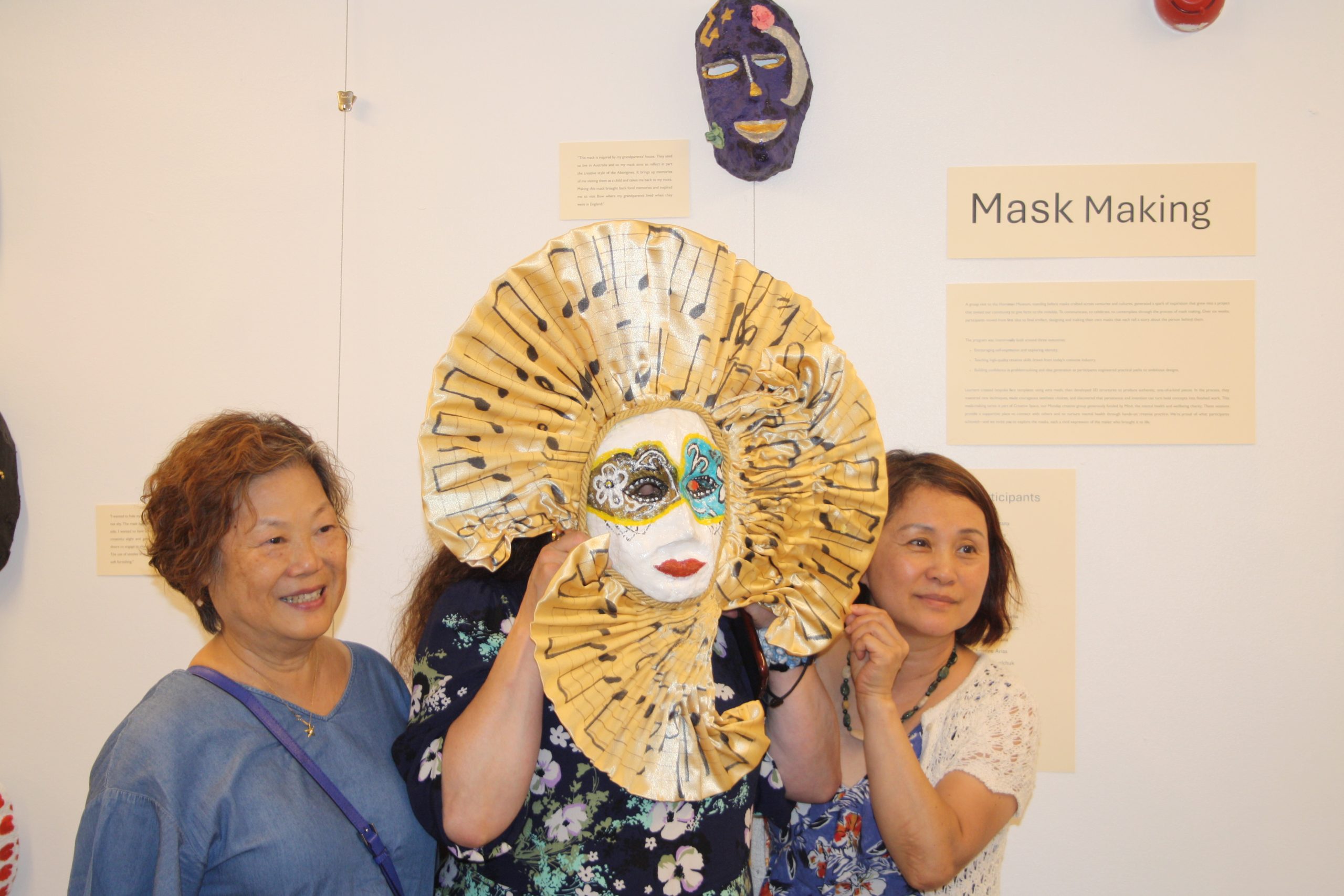 three women standing together, middle women holding large white mask over face